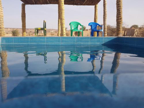 una piscina vacía con sillas coloridas reflejadas en el agua en Camping-Auberge du Puigaudeau et Aziza, en Atar