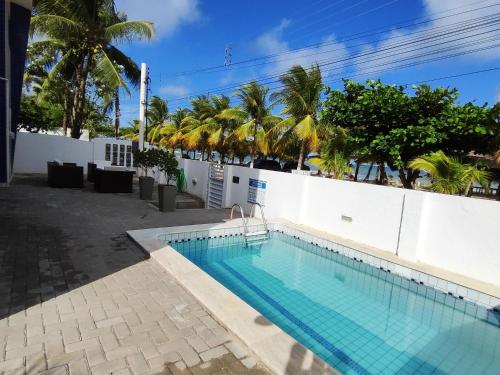 a swimming pool next to a white wall with palm trees at Flat Beira-Mar Maragogi in Maragogi