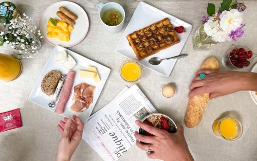 ロワシー・アン・フランスにあるAppart'City Collection Paris Roissy CDG Airportの雑誌を読む人々と朝食の食べ物を盛り付けたテーブル