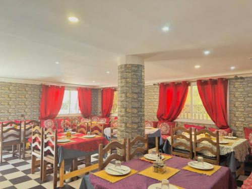 a restaurant with tables and chairs and red curtains at Hotel De La Vallée in Aït Baha