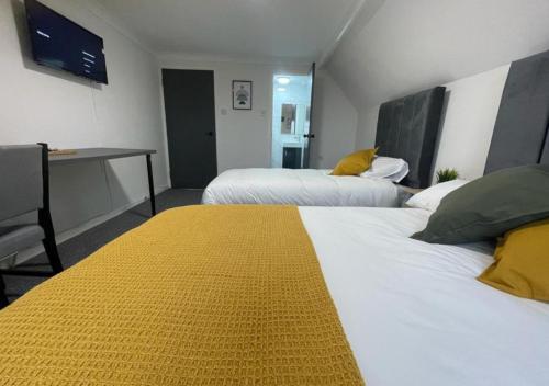a room with two beds with a yellow blanket on them at Woodford Hotel in London