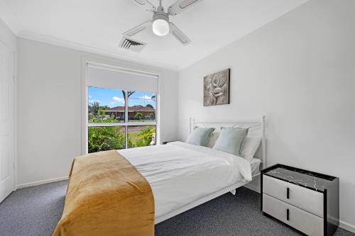a white bedroom with a bed and a window at Discover Mount Annan - Spacious 6-BR House in Narellan