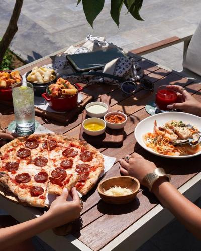 a wooden table with a pizza and plates of food at Pyra Hospitality West Pyramids Cairo in Cairo