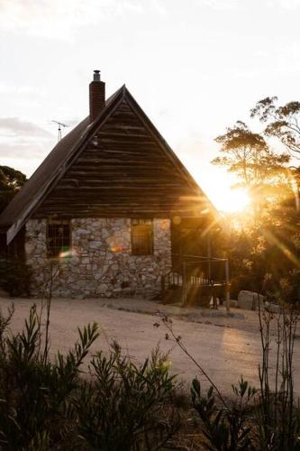 a stone house with the sun setting behind it at SABI Award Winning Designer Cabin in Binalong Bay