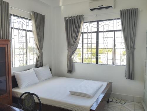 uma cama branca num quarto com duas janelas em Nhà Nghỉ SAO MAI em Hà Tiên