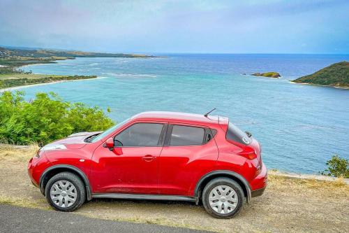 a red car parked on the side of a road near the ocean at Zen Cove w/rental vehicle access in Gros Islet