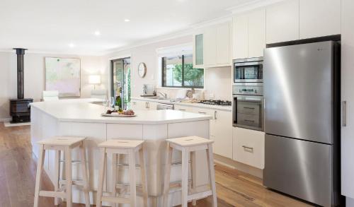 a kitchen with white cabinets and a refrigerator and stools at Weetaliba - Country Retreat in Yatte Yattah