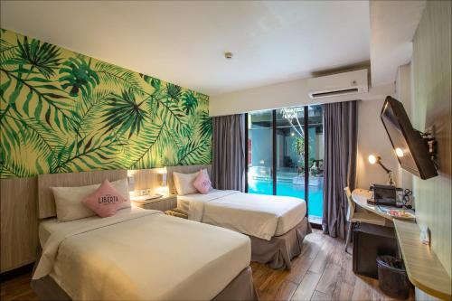 a hotel room with two beds and a desk at Liberta Seminyak Hotel in Seminyak