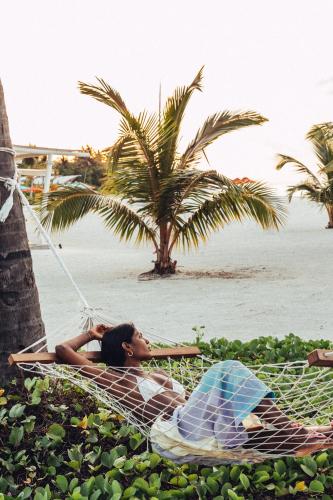 a woman laying on a hammock on the beach at Cinnamon Hakuraa Huraa Maldives - All Inclusive in Meemu Atoll