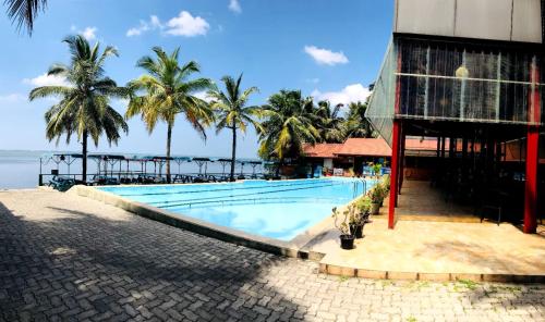 a swimming pool next to a building with palm trees at New Saniro Lagoon Deck in Katunayake
