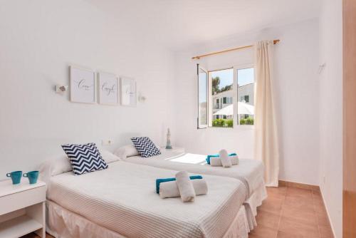 Duas camas num quarto branco com uma janela em Apartamentos Annabel's em Cala Galdana