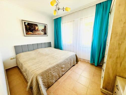 a bedroom with a bed with blue curtains and a window at Уютная квартира рядом с морем in Kemer