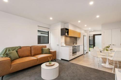 a living room with a brown couch and a kitchen at Style Location New Sunny 2Bdrms Free Park in Christchurch