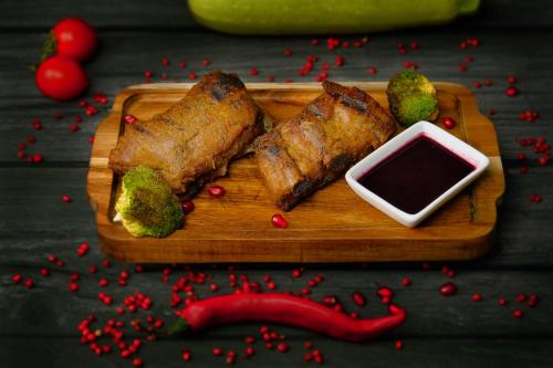 a wooden cutting board with meat and broccoli and a dipping sauce at VinoOdor - ვინოოდორ in Tʼelavi