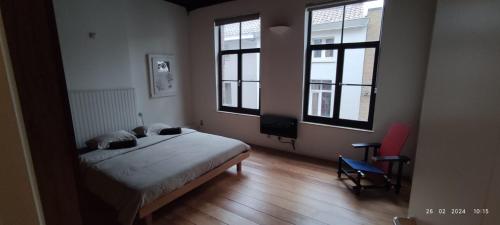een slaapkamer met een bed en 2 ramen en een stoel bij De Wijngaard in Gent
