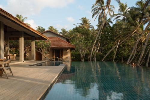 a swimming pool with a wooden deck next to a house at Kirana - A Santani Villa in Bentota