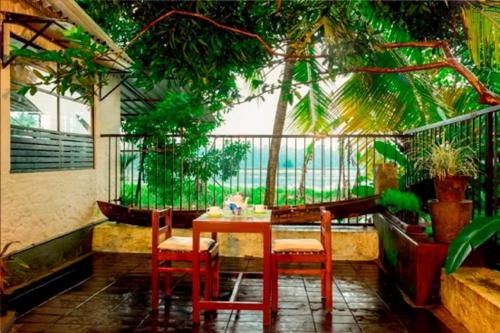 a table and chairs on a balcony with trees at Riverdale Homestay Kumarakom by LexStays in Kumarakom