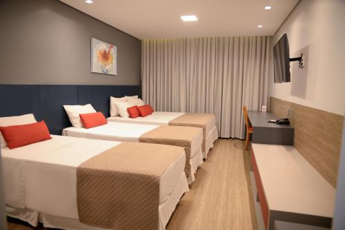 a hotel room with three beds and a desk at Carlton Plaza Hotel Uberlandia in Uberlândia