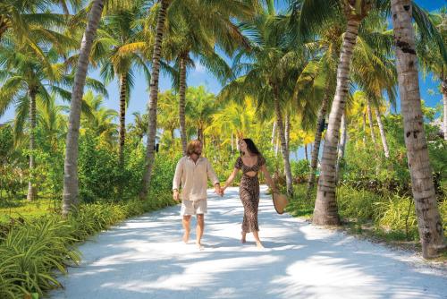 a man and woman walking down a palm tree lined path at OBLU XPERIENCE Ailafushi - All Inclusive with Free Transfers in Male City
