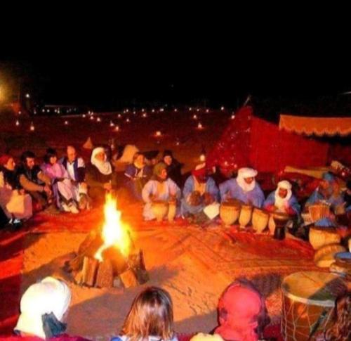 eine Gruppe von Menschen, die in einem Zirkus um ein Feuer herum sitzen in der Unterkunft Merzouga Luxurious Camp in Merzouga