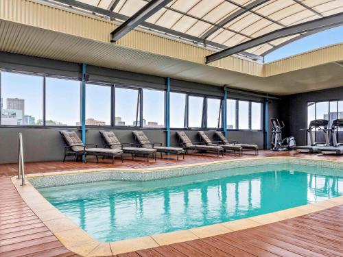 une grande piscine avec des chaises et des fenêtres dans l'établissement Mantra on Hay Perth, à Perth