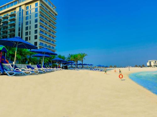 a beach with chairs and blue umbrellas and a building at Marjan Island Beautiful Apartment Sea View Beach Luxury Rooms Ras Al Khaimah UAE in Ras al Khaimah