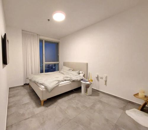 a white bedroom with a bed and a window at Gindi Tower Apartments TLV in Tel Aviv