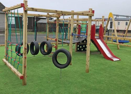 a playground with swings and slides on the grass at Ryan Bay in Dunragit