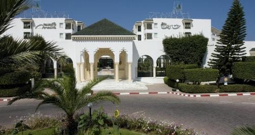 a white building with a courtyard with trees and plants at El Mouradi Palm Marina - Couple et Famille uniquement in Port El Kantaoui