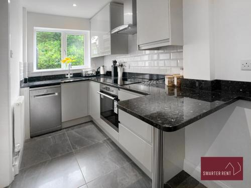 a kitchen with white cabinets and a black counter top at Guildford - 2 Bedroom House in West Clandon