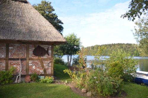 a hut with a grass roof next to a lake at Reetdachkate auf Gestüt Schierensee in Grebin