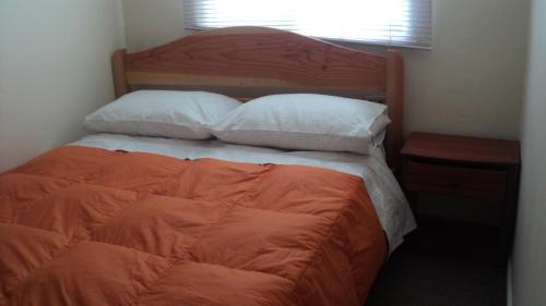 1 cama con edredón de naranja y 2 almohadas en Departamentos Arlenne II, en Valdivia
