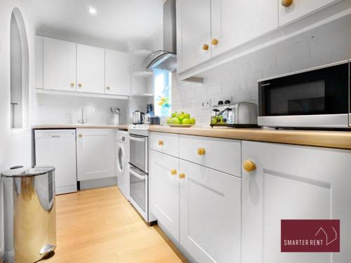 La cuisine est équipée de placards blancs et d'un four micro-ondes. dans l'établissement Bracknell - Modern, Spacious 1 Bedroom House, à Easthampstead