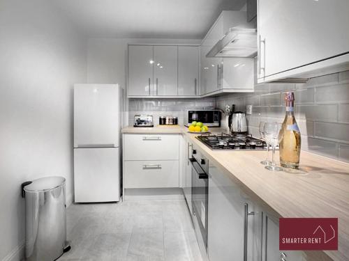uma cozinha com armários brancos e um frigorífico branco em Wokingham - 2 Bed Modern House - Parking em Wokingham