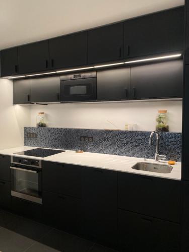- une cuisine avec des placards noirs et un évier dans l'établissement Cosy appartement 3min de Paris, à Levallois-Perret