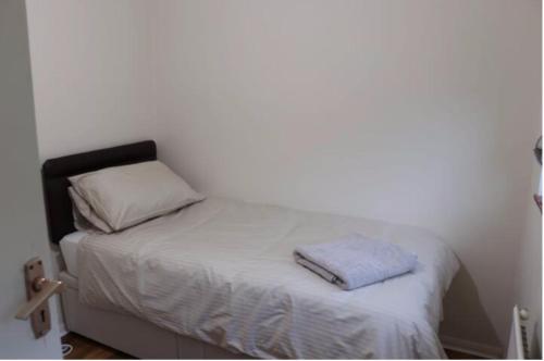 a small bed in a white room with a pillow at Wellesley, Central London Living in peaceful Suburb in Kenley