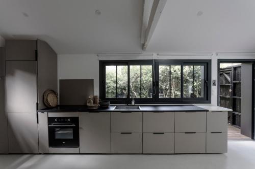 a kitchen with white cabinets and a sink and windows at PYLA: Nice creative studio 200 m from the beach in La Teste-de-Buch