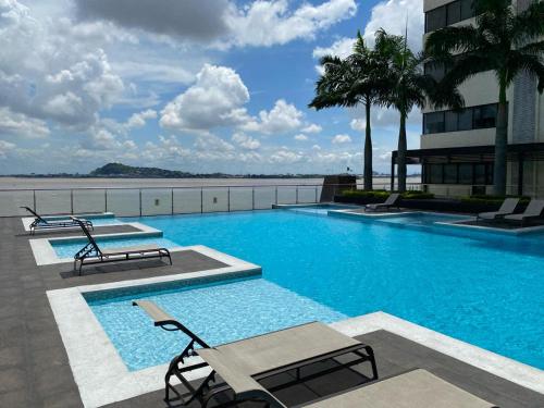 una piscina con 2 sillas y un edificio en Puerto Santa Ana, Torres Bellini, 2 dormitorios, Parqueo en Guayaquil