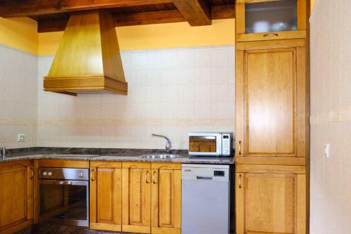 cocina con armarios de madera, fregadero y microondas en La Bolera Paraíso Astur en Llanes