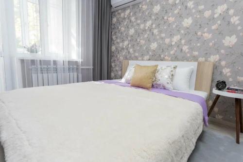 a bedroom with a white bed and a floral wall at Уютная студия в центре in Almaty
