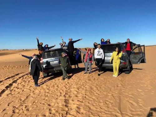 a group of people standing next to a truck in the desert at GITE Take your time in Merzouga