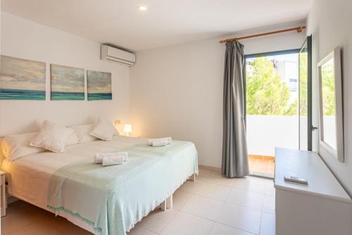 a white bedroom with a bed and a large window at Apartamentos Es Dolç in Colònia de Sant Jordi