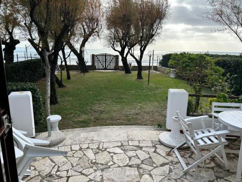 eine Gruppe von weißen Stühlen, einem Tisch und Bäumen in der Unterkunft Fronte Mare Villa Acquasanta zona "LA FIUMETTA" Terracina in Terracina