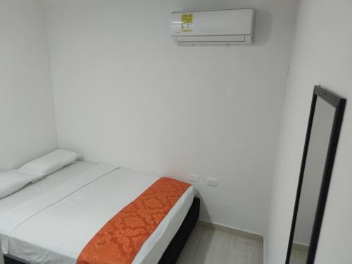 a white bedroom with a bed with an orange blanket at Cabaña Gaia Rodadero in Santa Marta