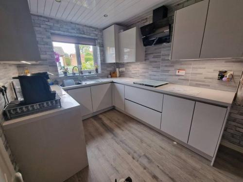 a kitchen with white cabinets and a wooden floor at Spacious 3bed semi/Gamesroom/Drive/10mins to City in Wrexham