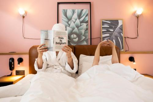 a woman laying in bed reading a newspaper at Hotel Indigo Antwerp City Centre by IHG in Antwerp