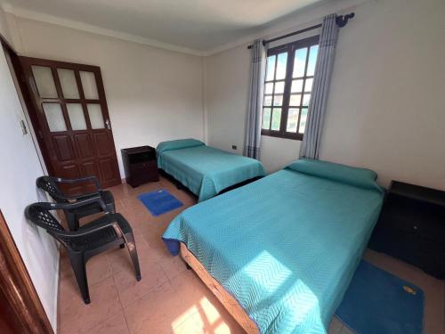 a bedroom with two beds and a chair and a door at Casa Amigable y Confortable in Yacuiba