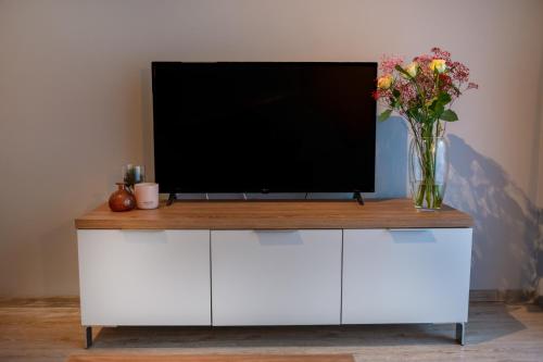a tv on a white cabinet with a vase of flowers at Sunset A23 przy plaży in Pobierowo