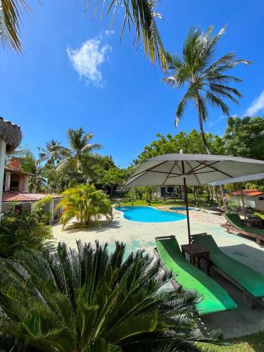 a resort with a pool and an umbrella and palm trees at Pousada Les Alizes in Icaraí