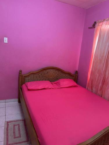 Cama en habitación con pared de color rosa en Casa Fransina, en Blue Bay